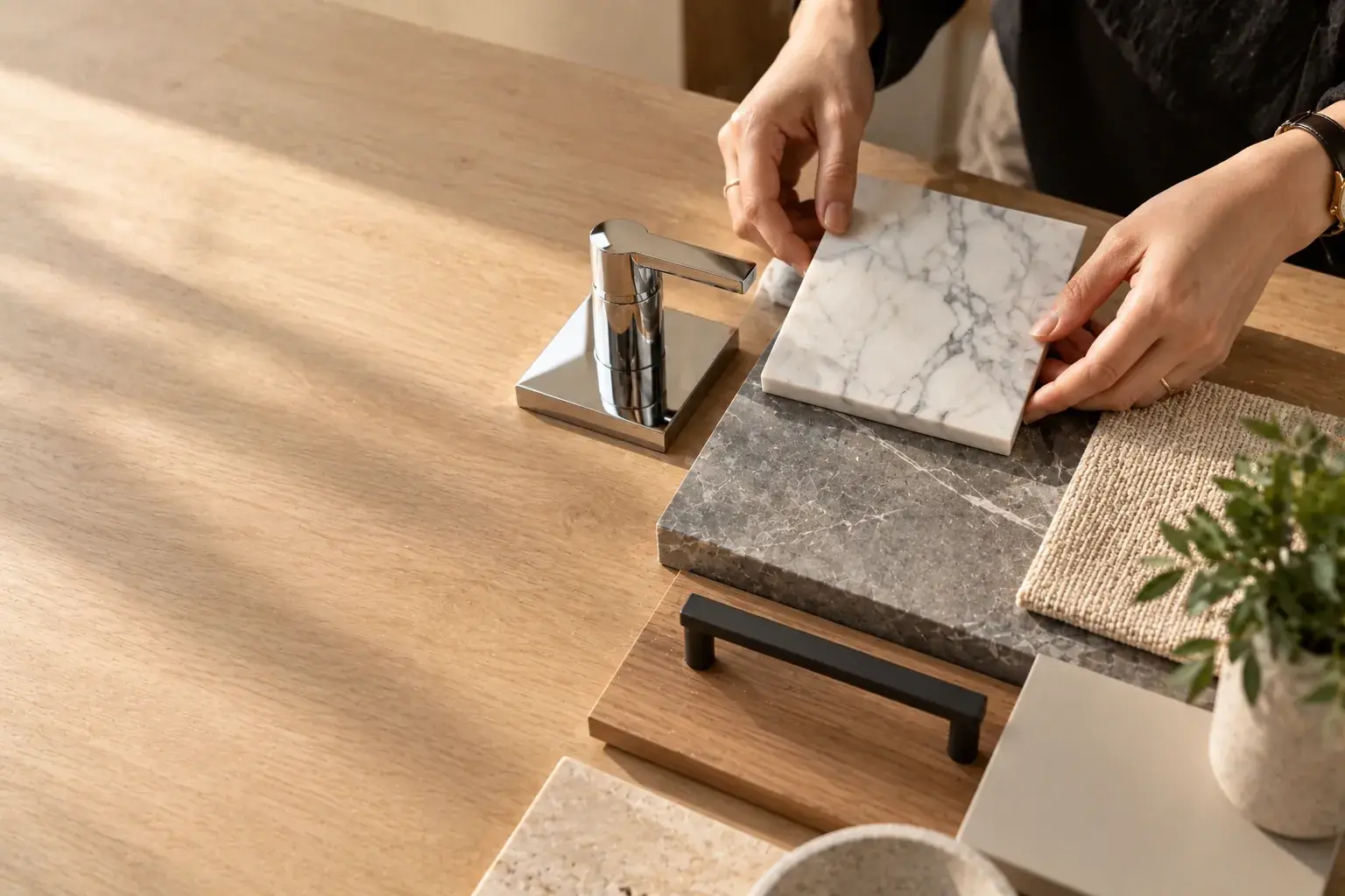 Designer's hands arranging marble, stone, chrome and fabric finish samples on an oak table